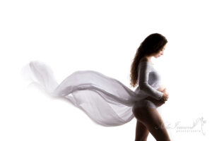 Future maman en sous-vêtements blancs, enveloppée d'un tissu vaporeux, pose de profil. Séance photo de grossesse près de Montpellier.