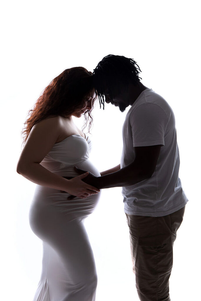 Silhouette de futurs parents enlacés, le ventre rond de la future maman bien visible. Un moment de tendresse capturé lors d'une séance photo de maternité, témoignant de l'amour et de l'impatience suscités par la séance photo.