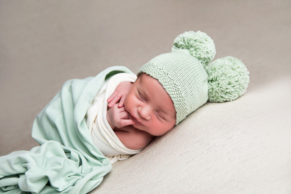 Nouveau-né endormi, emmitouflé dans une couverture douce et portant un bonnet vert tricoté à pompons, idéal pour la photographie de nouveau-né. Photos de bébé paisibles.