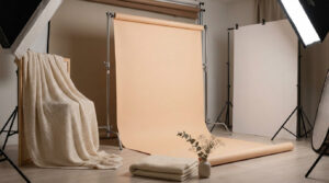 Choisir le meilleur fond photo studio pour vos séances Studio photo professionnel équipé d'un fond en papier beige, d'un plaid en laine et d'éclairages sur trépieds.