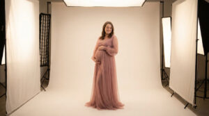 Quel budget prévoir pour une séance photo de grossesse en studio Une femme enceinte souriante porte une robe rose poudrée dans un studio photo professionnel avec des éclairages.